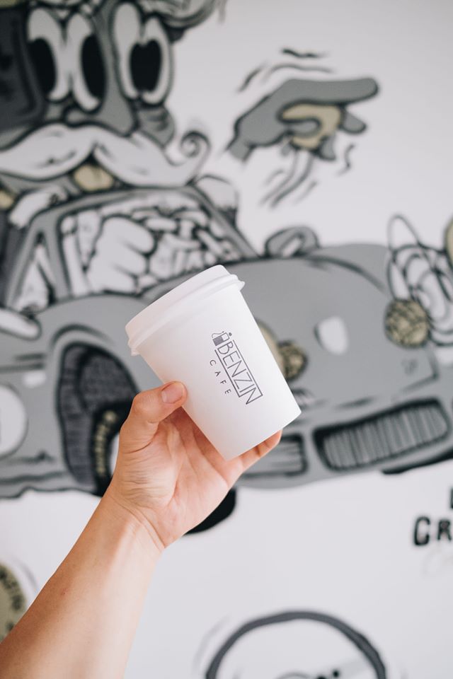 White takeaway coffee cup with Benzin Café branding, set against a mural background, highlighting creative packaging that merges branding with functionality.