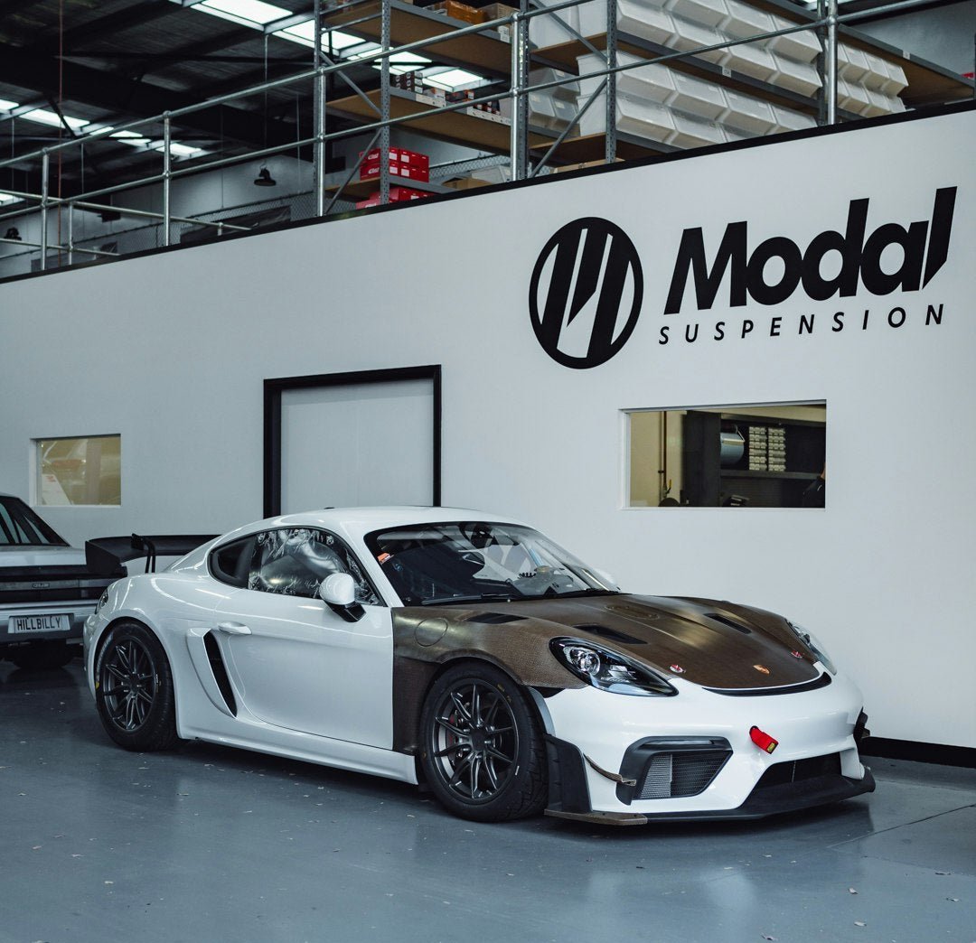 White Porsche Cayman GT4 at Modal Suspension garage, highlighting automotive upgrades and suspension enhancements.